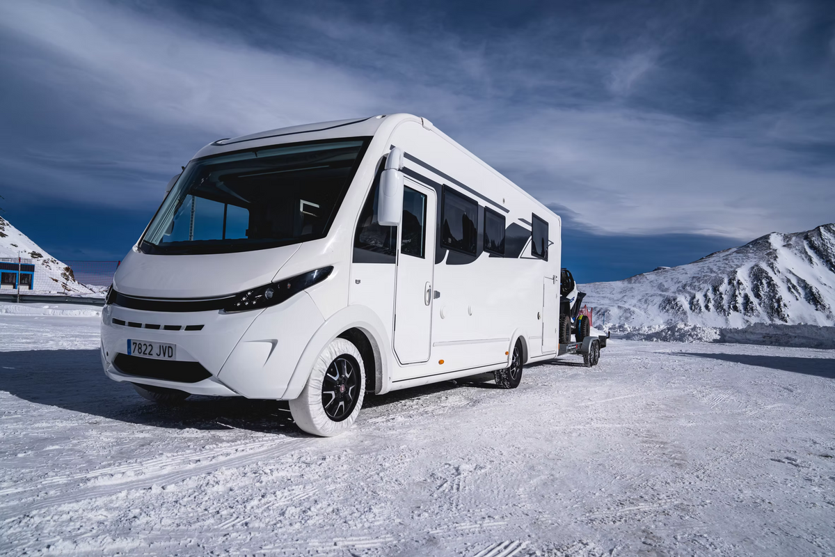 White van with a trailer on a snowy landscape under a blue sky